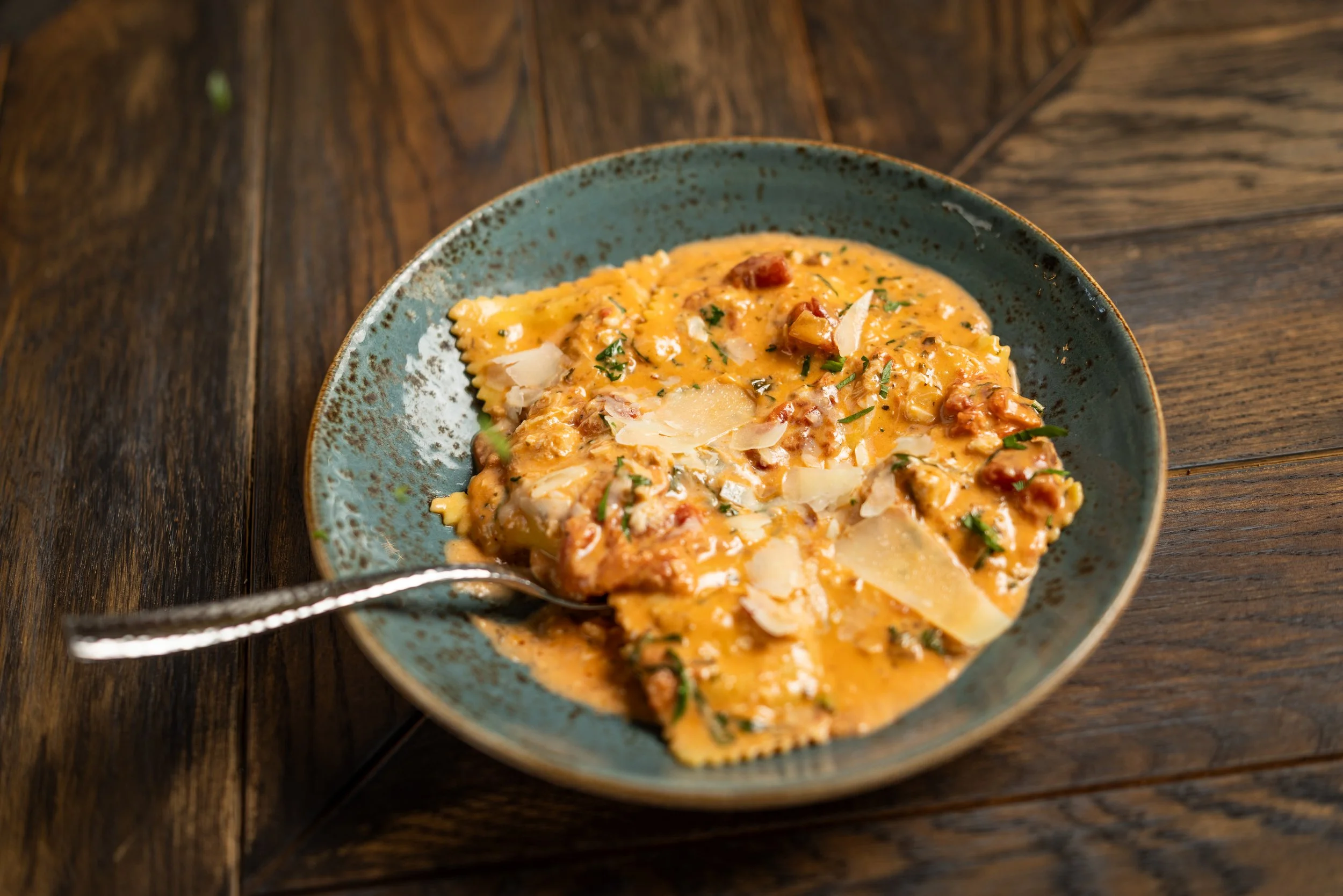 A bowl of creamy pasta with cheese, herbs, and bits of meat on a rustic wooden table.