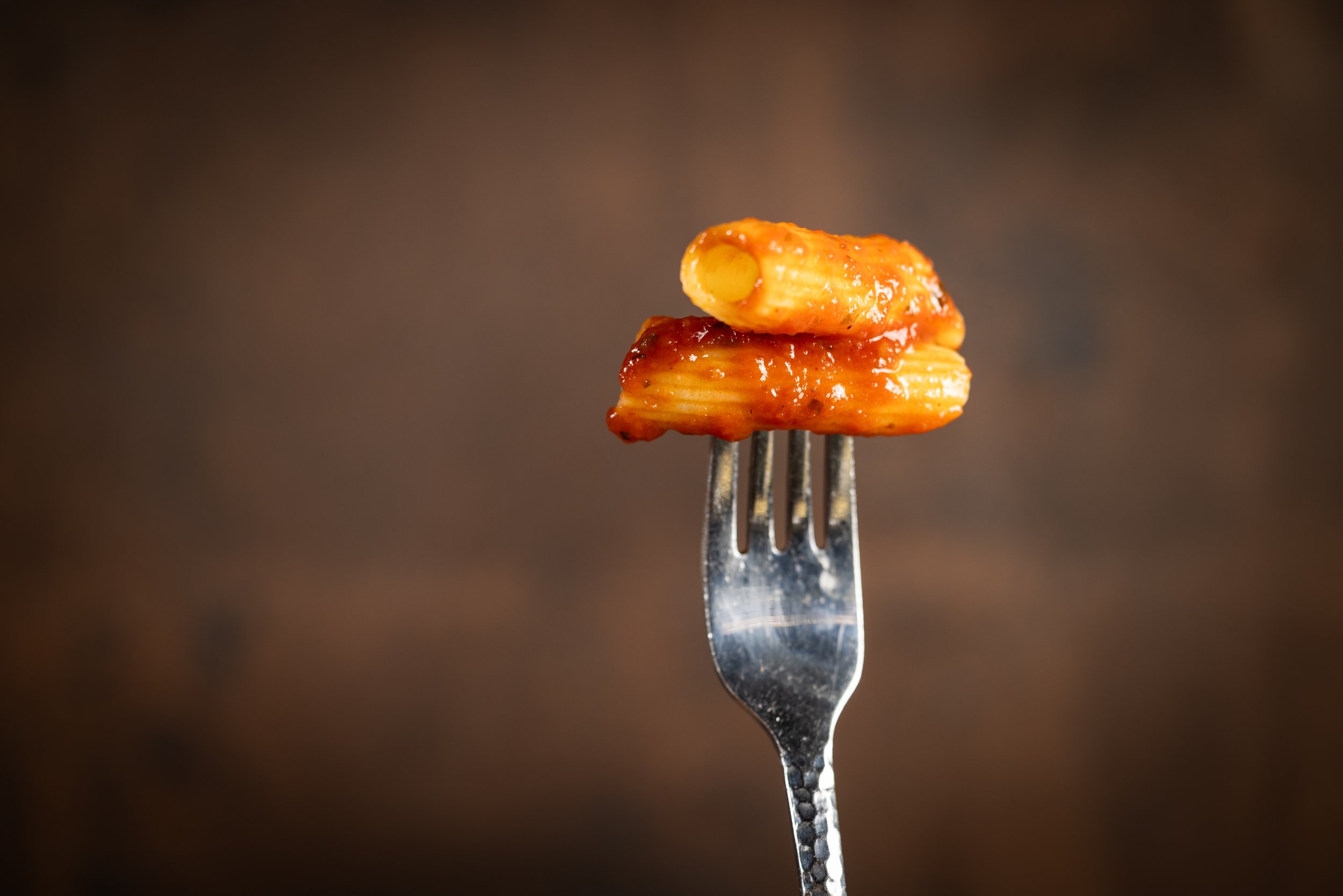 Close-up of a fork holding a piece of pasta with tomato sauce against a dark background.