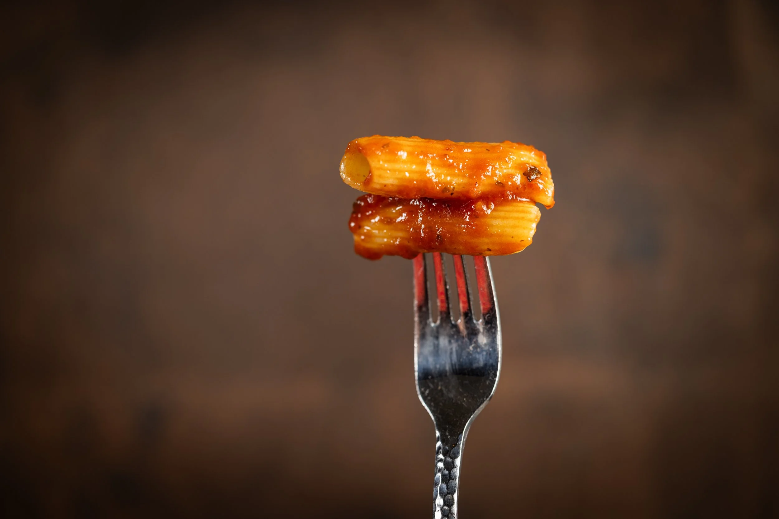 Close-up of a fork with a piece of cooked pasta covered in red sauce against a dark background.