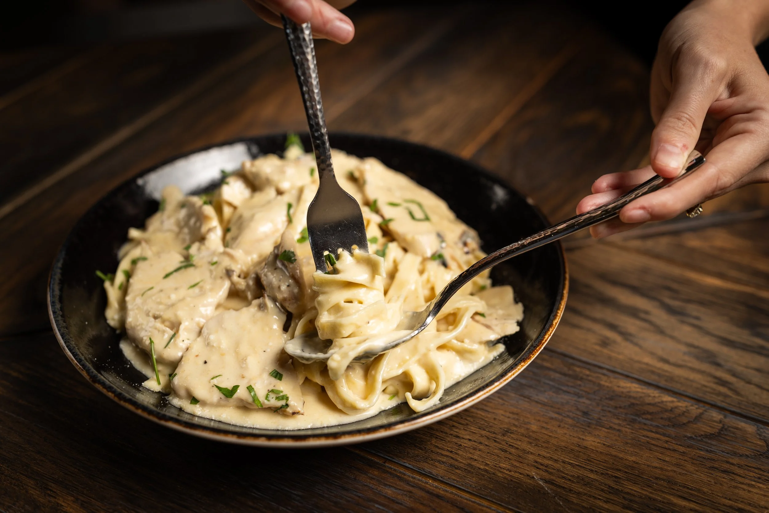 A bowl of creamy pasta with herbs, being served with a fork by a person.