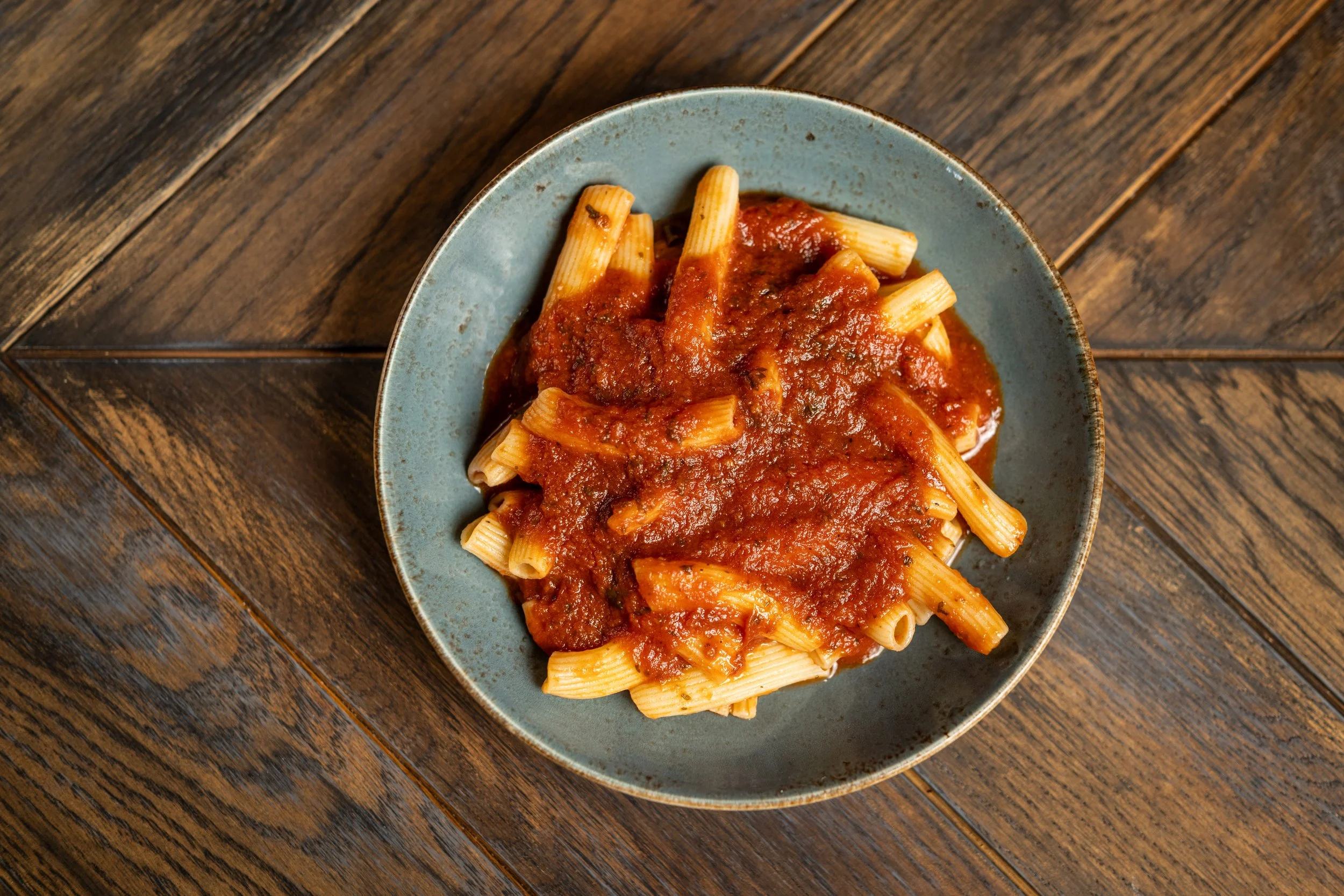 A bowl of cooked rigatoni pasta with tomato sauce on a wooden table.