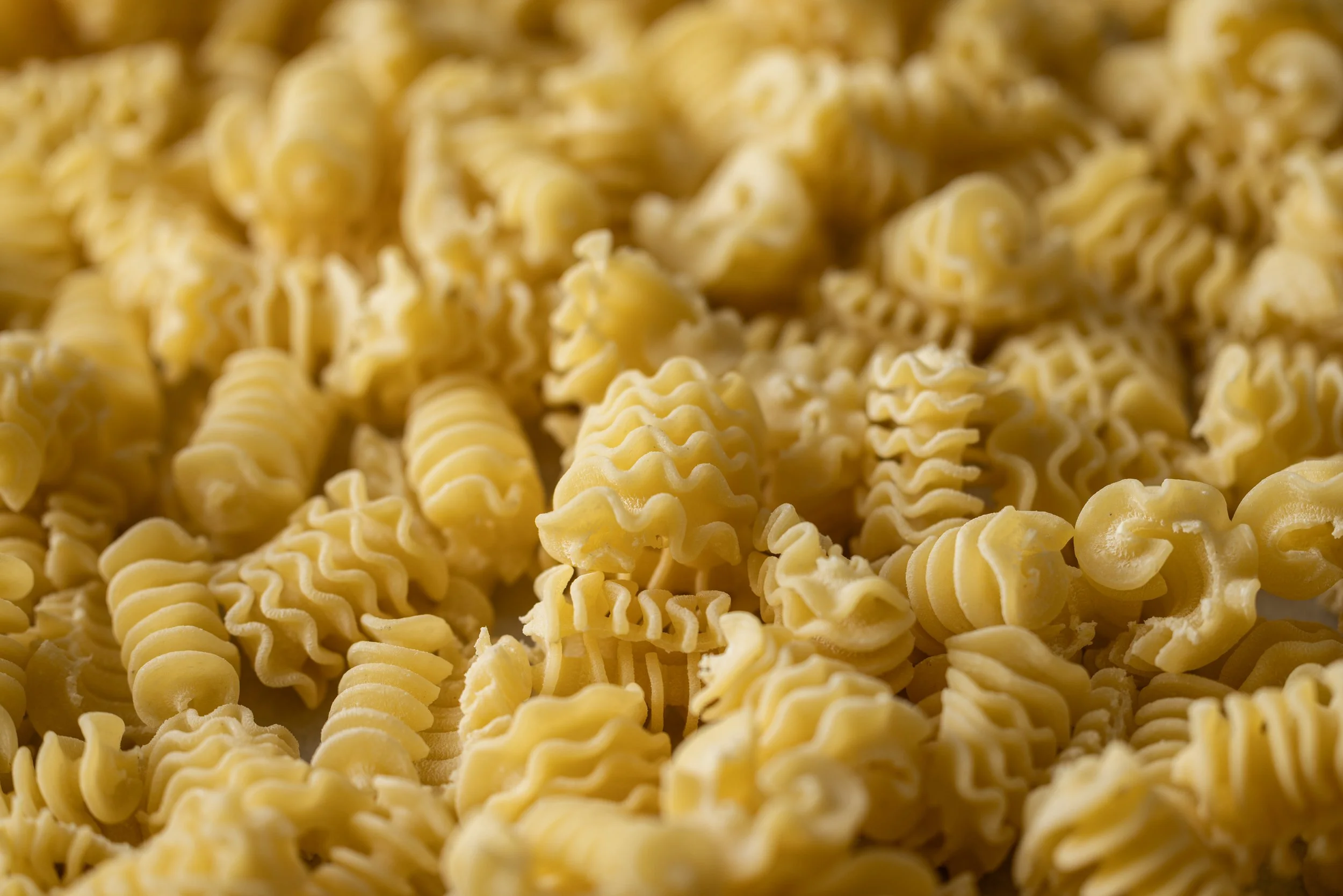Close-up of yellow uncooked curly pasta noodles with a textured, ridged surface.