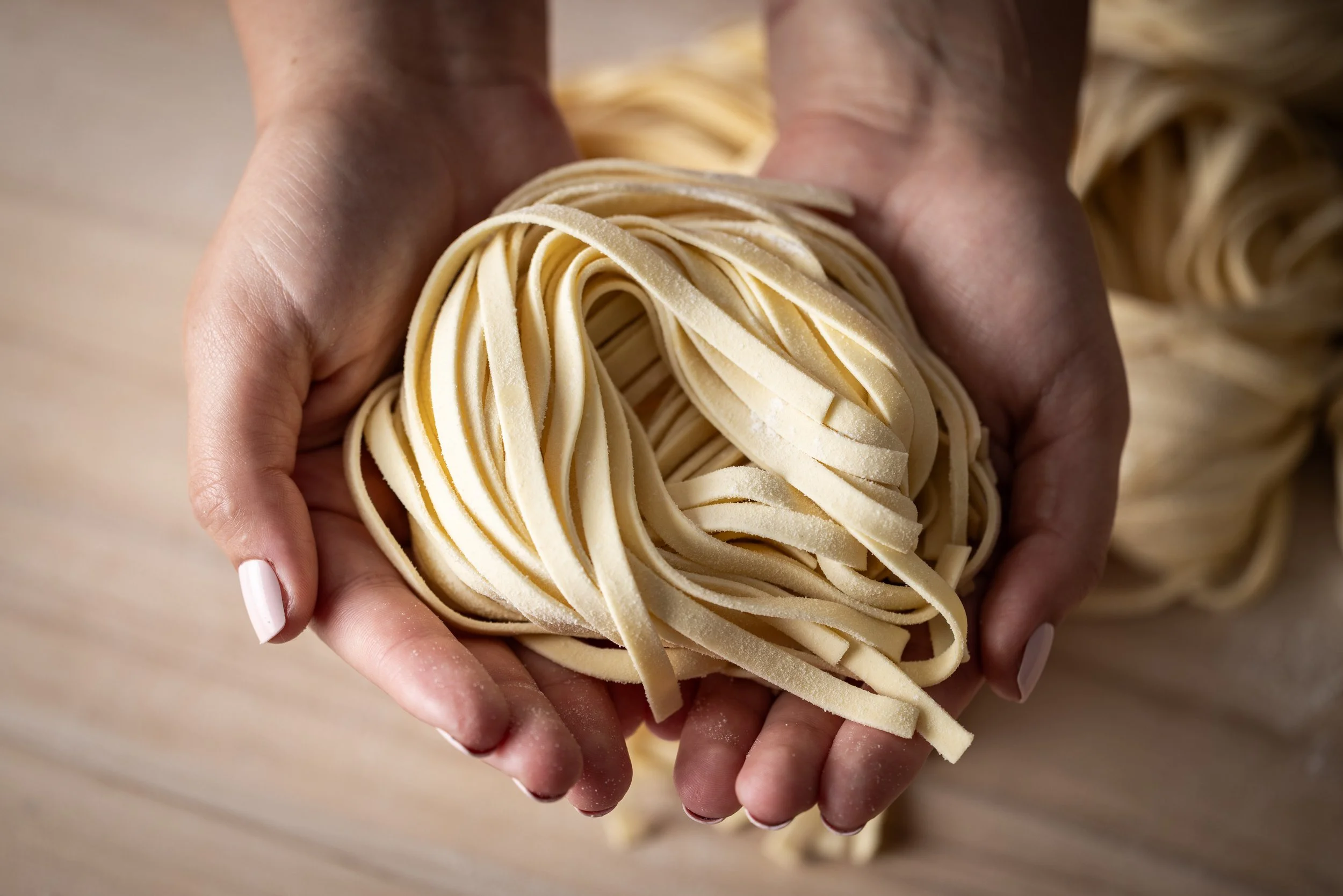 Close-up of hands holding fresh, uncooked fettuccine pasta.