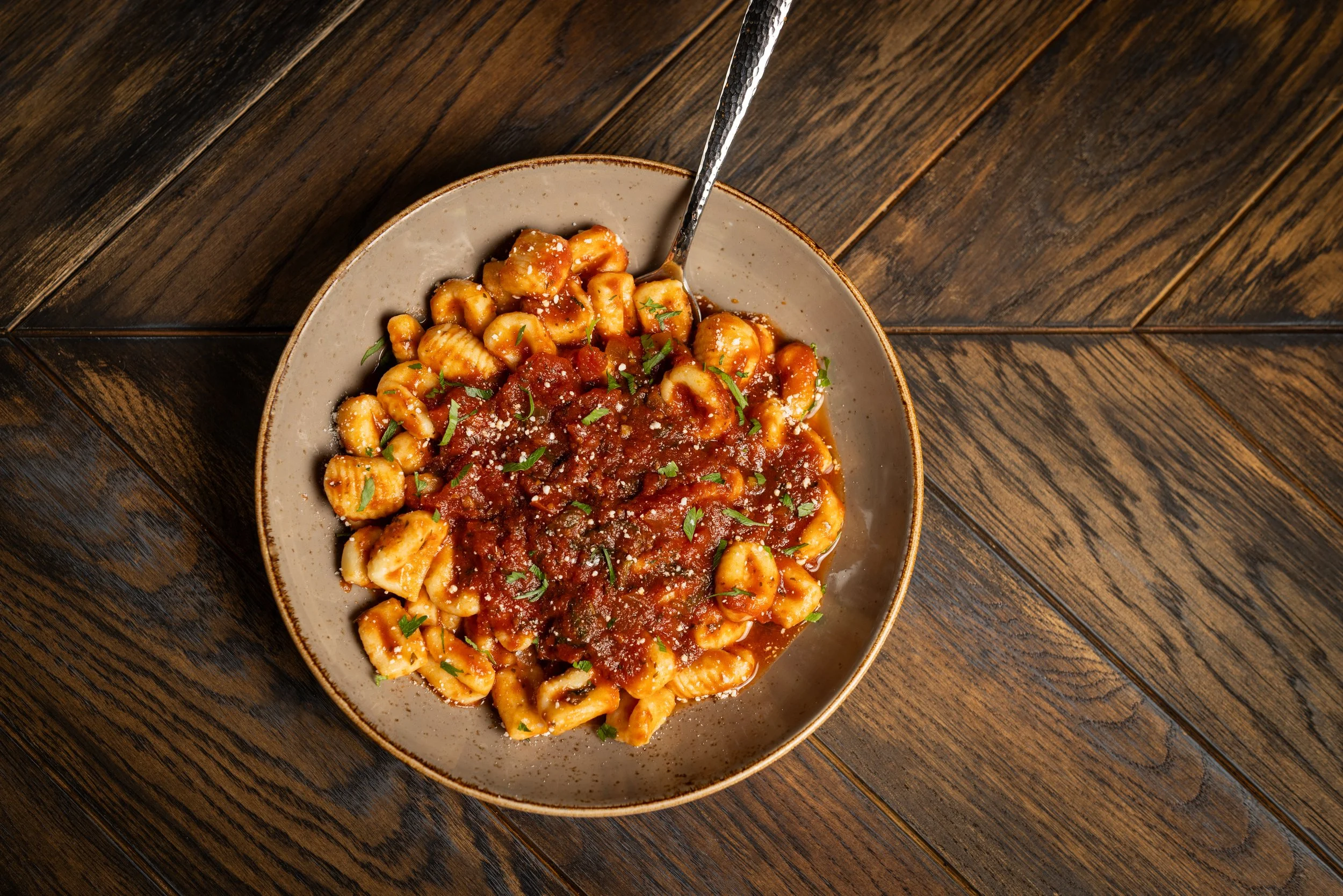 A bowl of pasta with tomato sauce, herbs, and grated cheese on a wooden table.