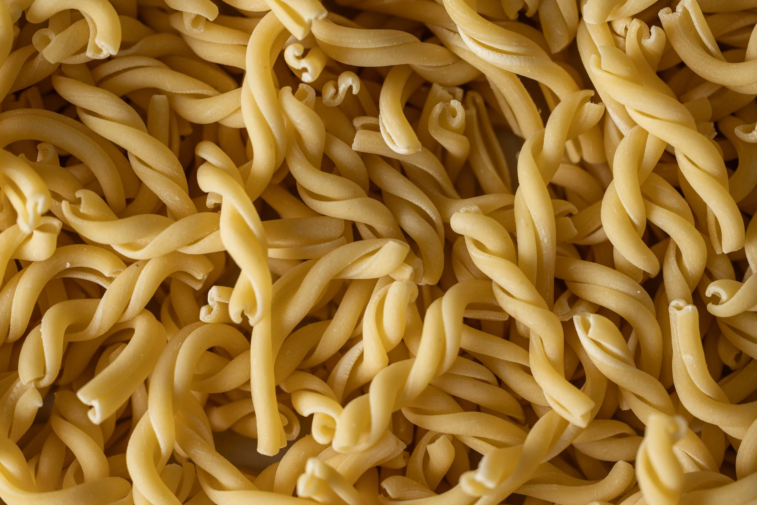 Close-up view of uncooked, yellow twisted egg noodles.