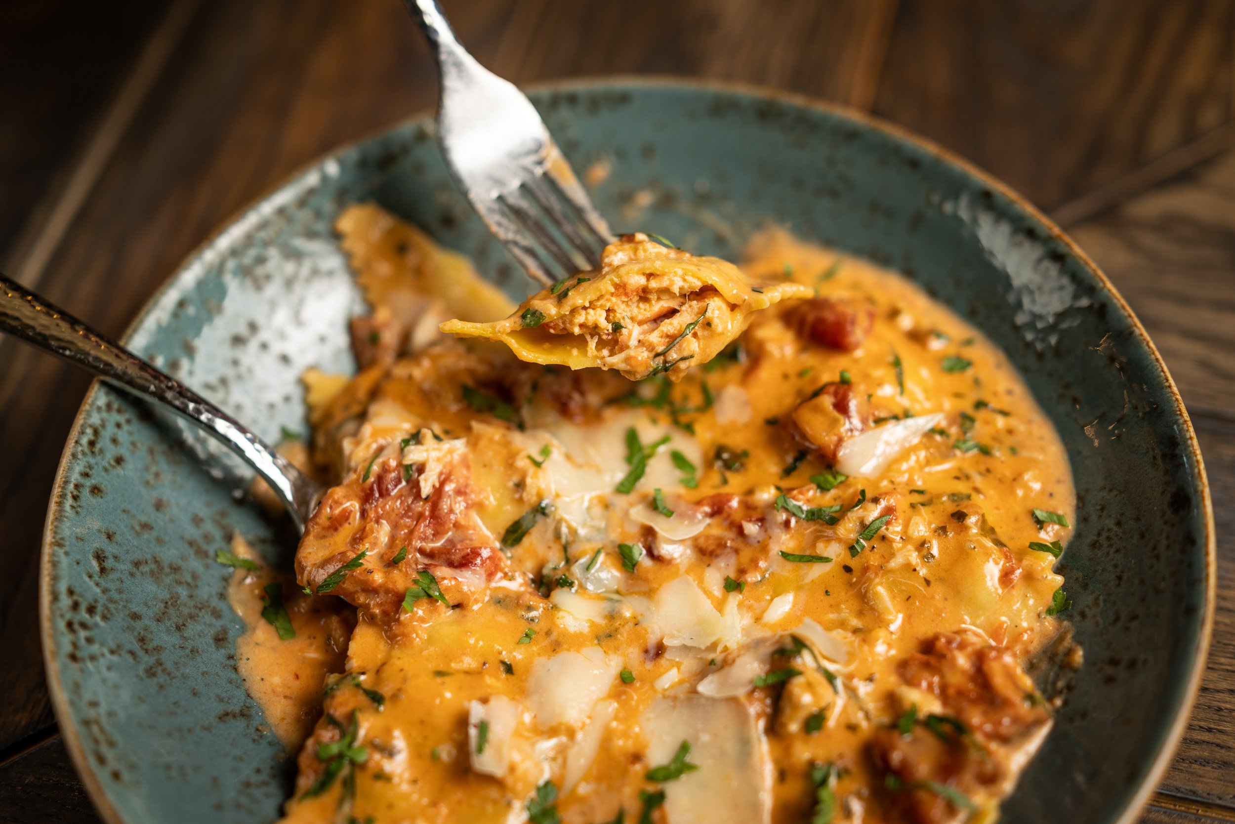 A bowl of creamy baked pasta topped with chopped herbs and cheese, with a fork lifting a portion.