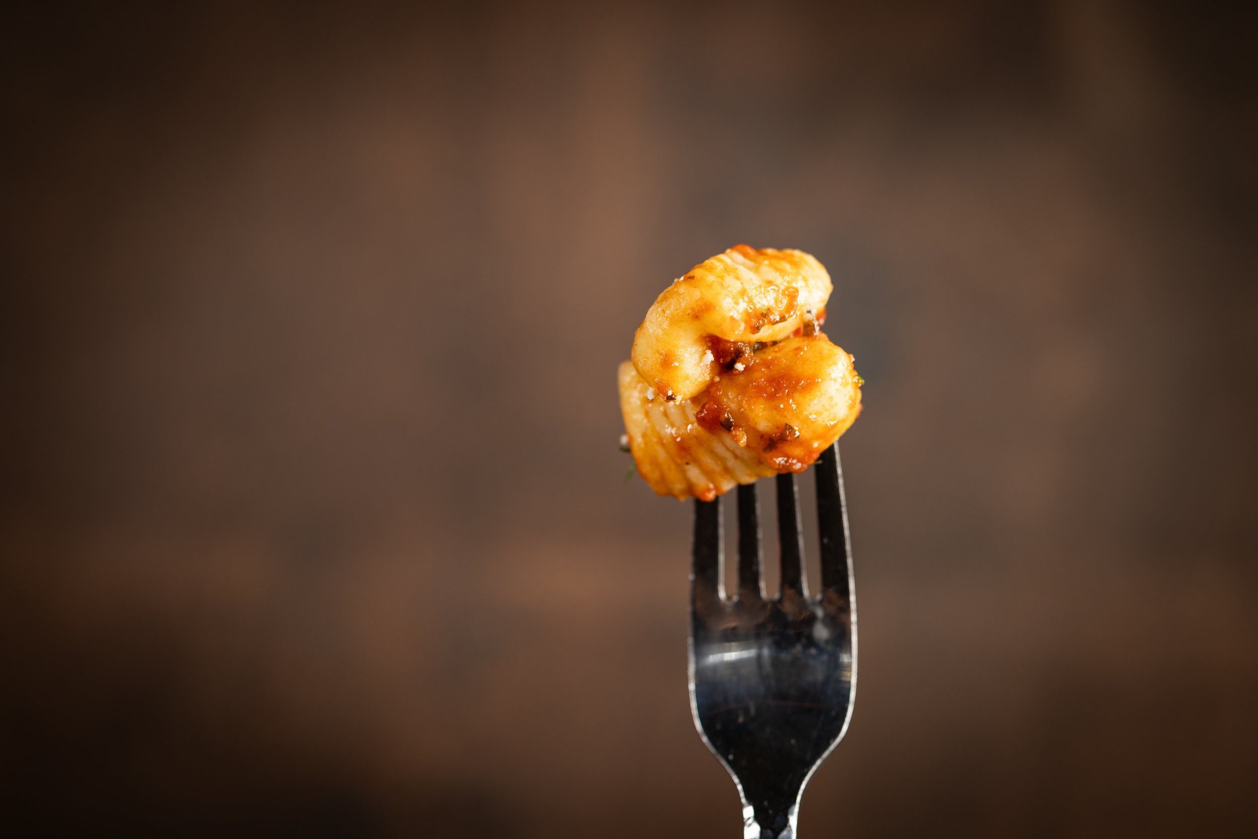 Close-up of a fork holding a cooked shrimp with sauce, with a dark blurred background.
