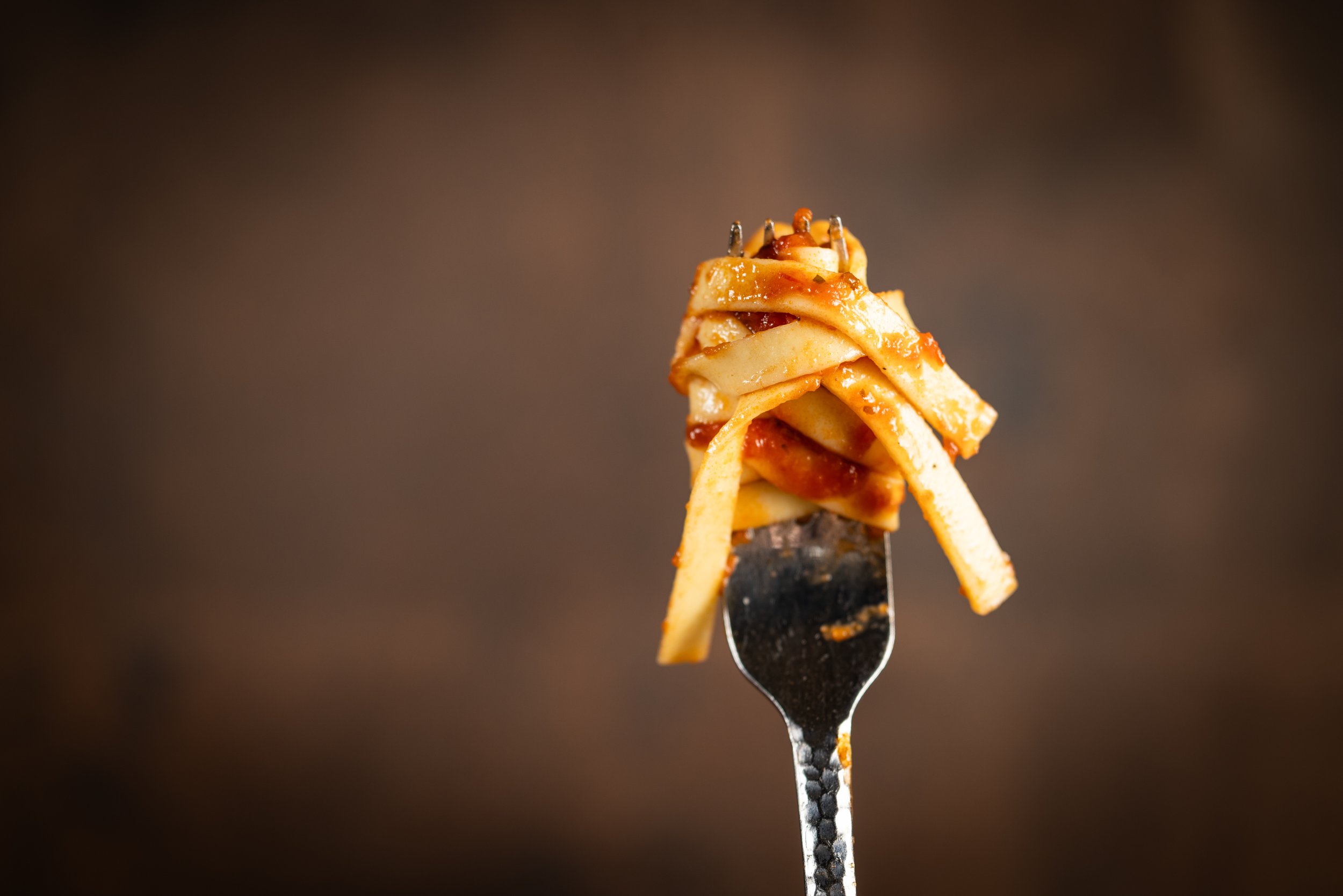 A close-up of a fork with cooked pasta topped with tomato sauce and herbs against a dark background.