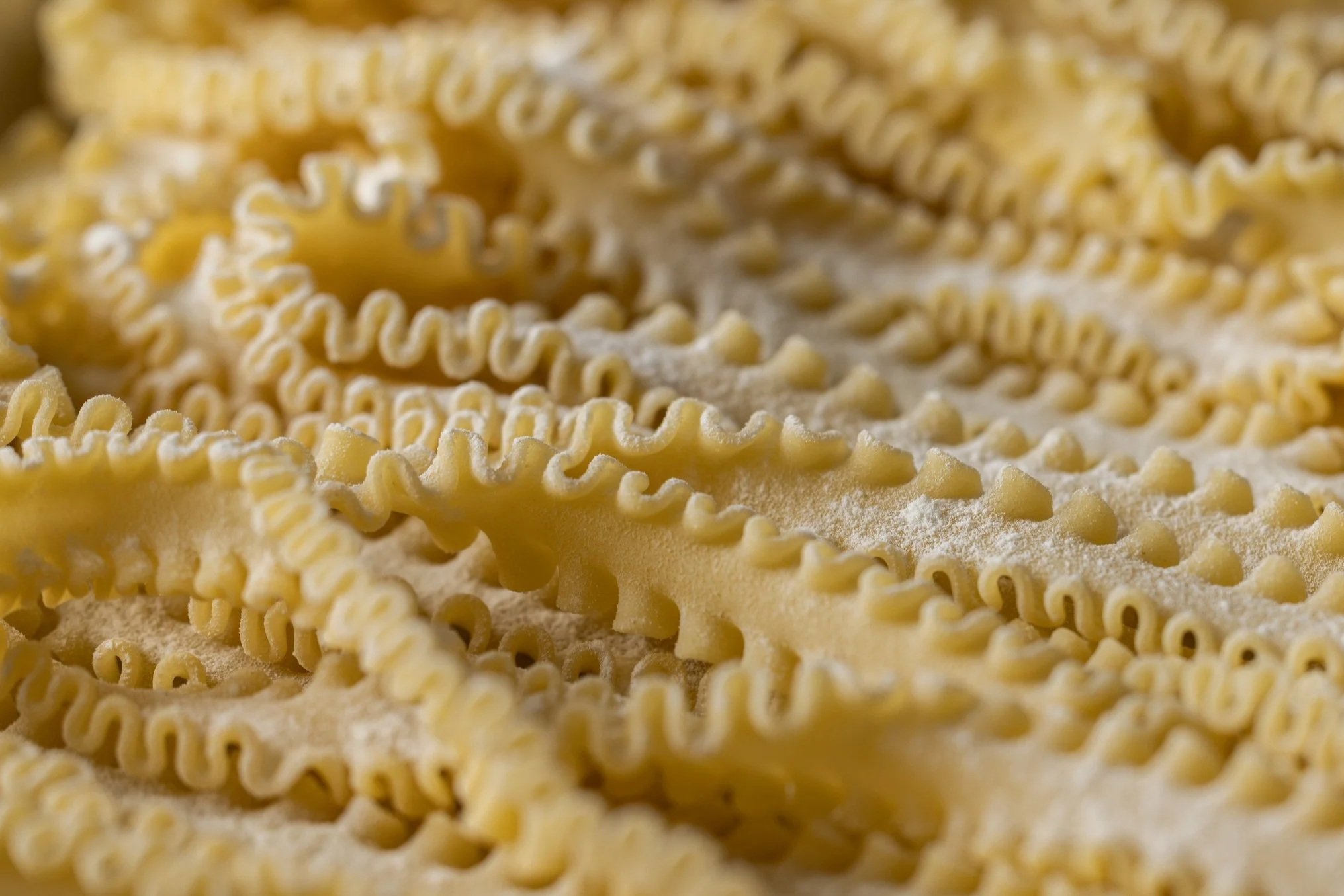 Close-up of uncooked curly yellow pasta noodles layered on a surface.