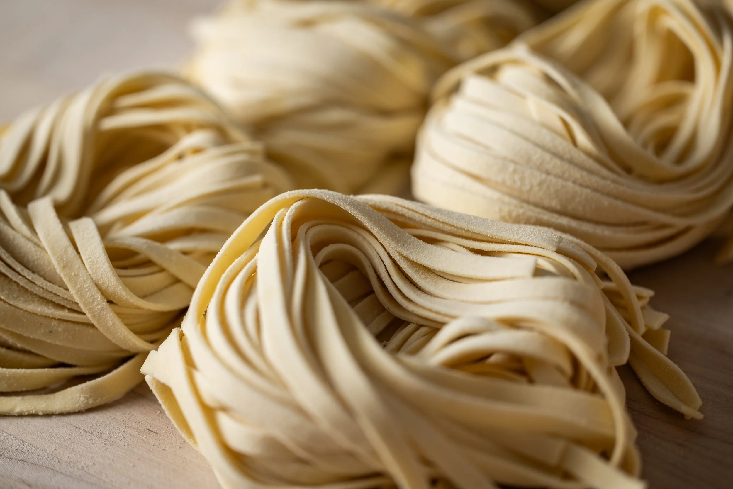 Close-up of fresh, uncooked pasta nests on a wooden surface.