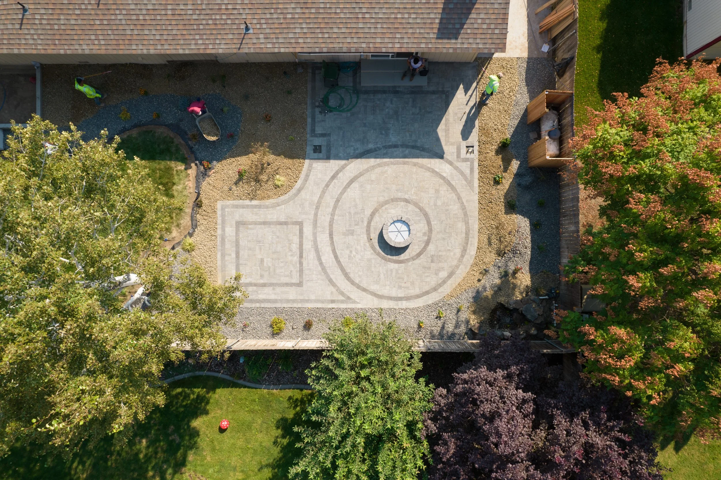 An aerial view of a backyard with a patio, landscaping, trees, and some workers installing or maintaining the yard.