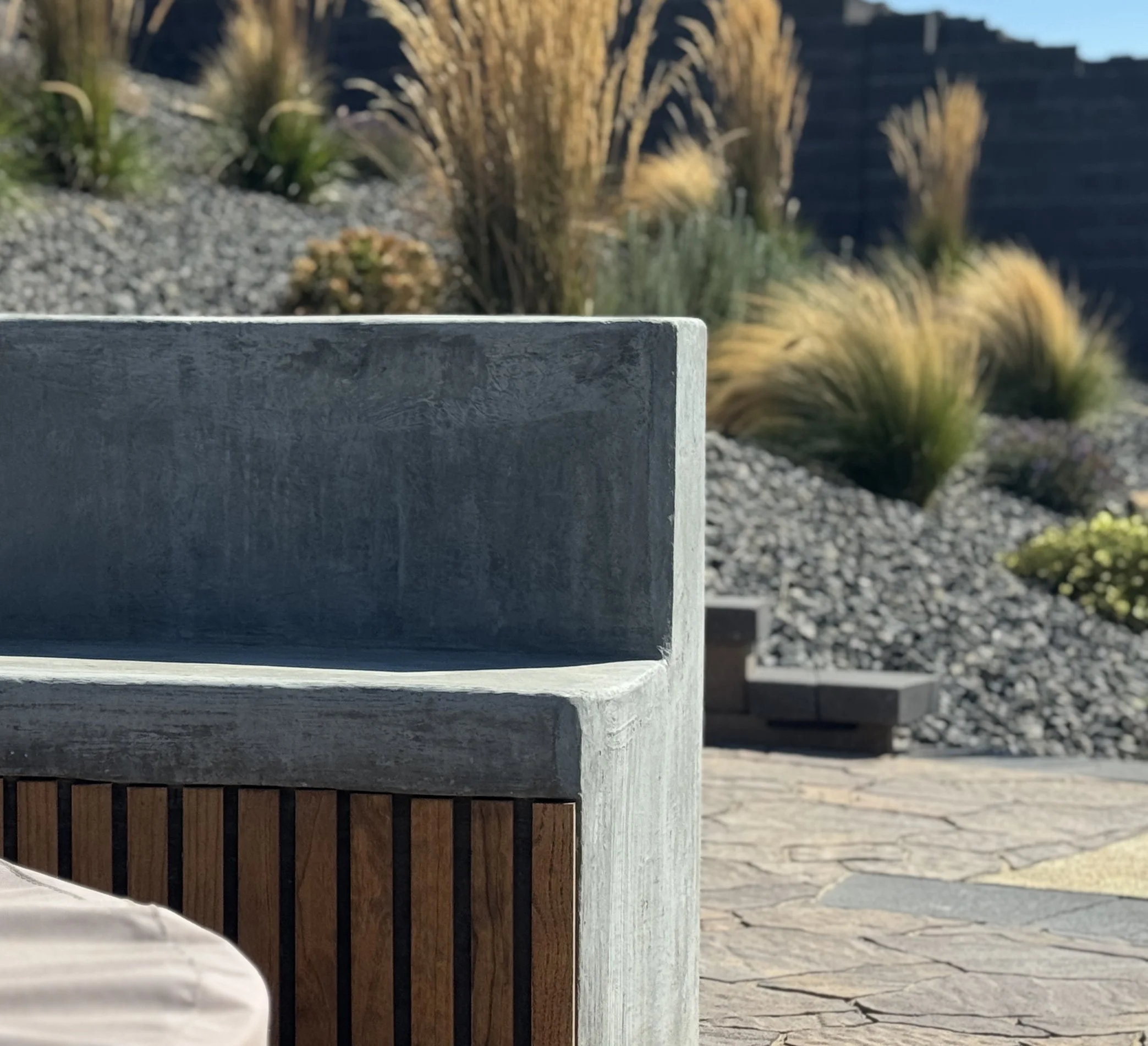 Close-up image of a concrete and wood bench with rocks and desert plants in the background.