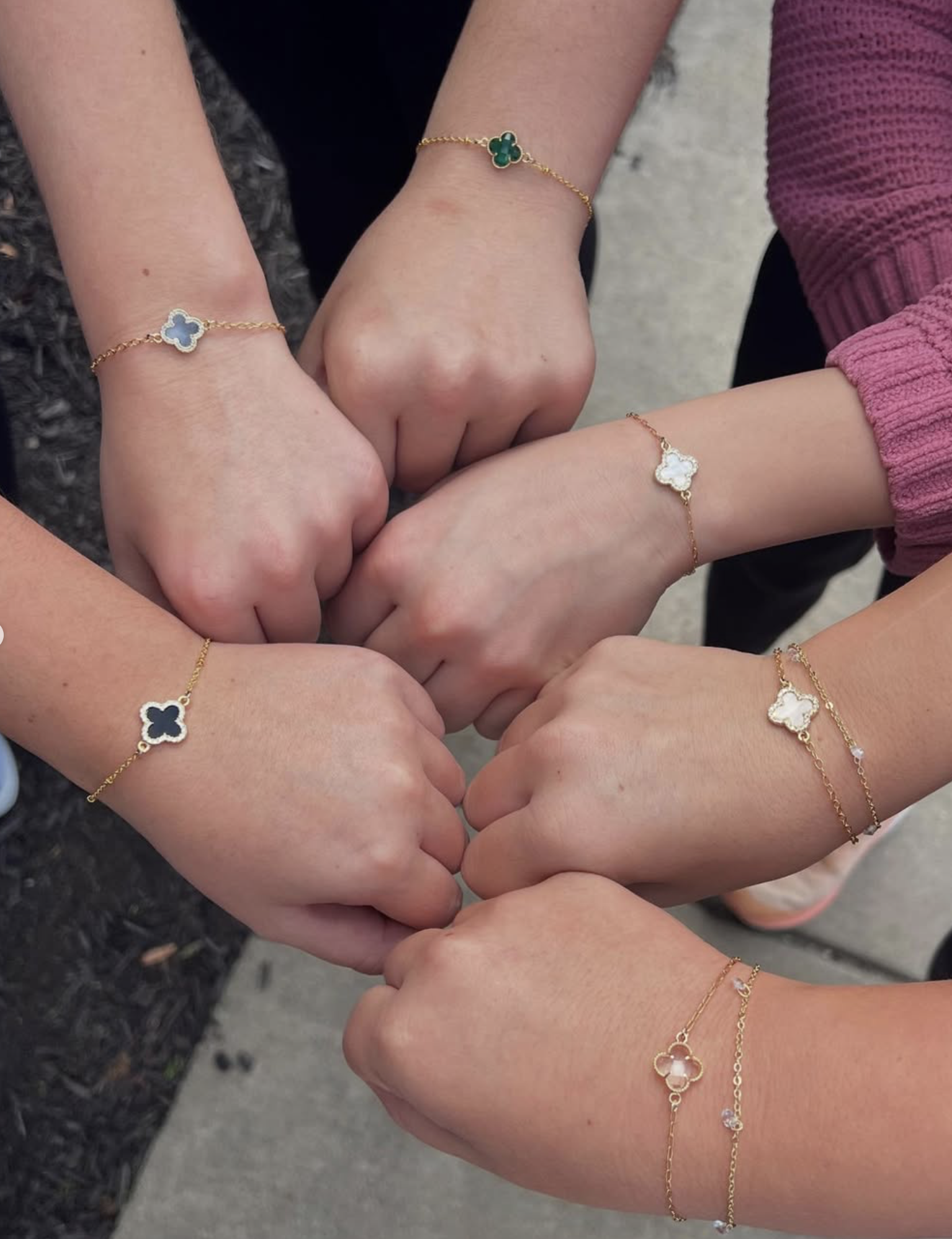 Multiple hands with matching gold and gemstone bracelets forming a circle.