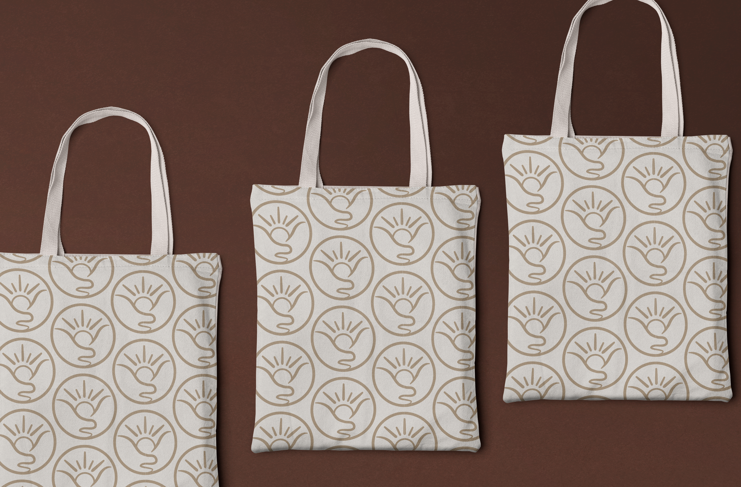 Three tote bags with a beige pattern of a stylized sun design, arranged on a brown surface.