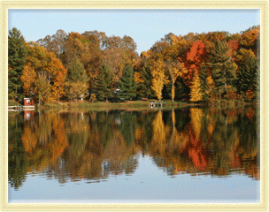 Autumn trees with colorful fall foliage reflected in a calm lake with a small dock in the distance.
