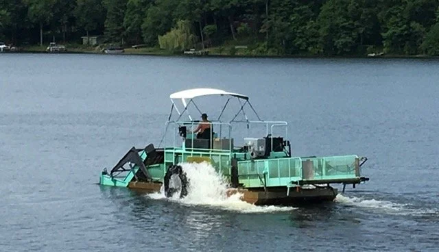 A pontoon boat with an open deck and a white canopy floating on a lake.