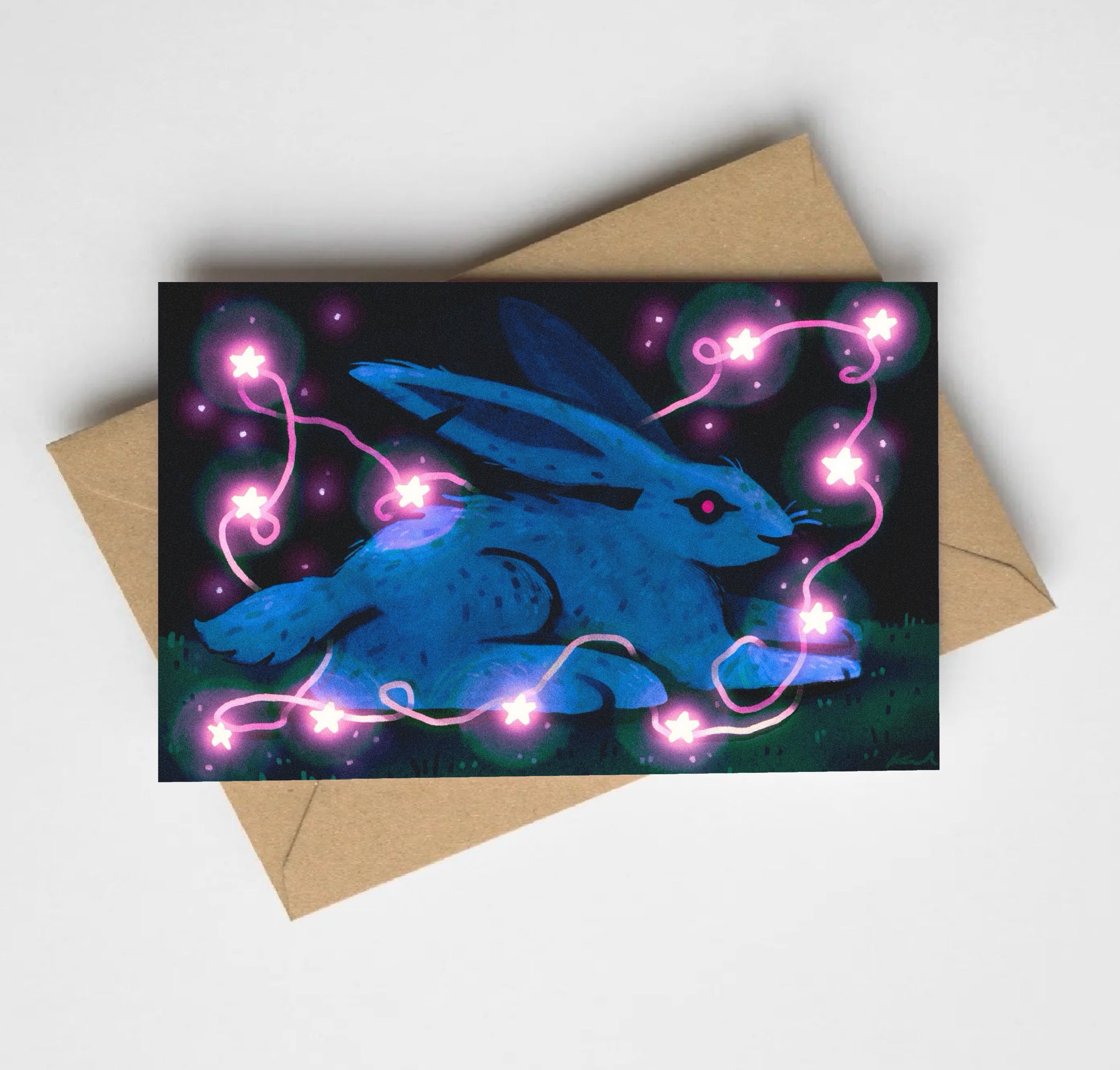 Close-up of a colorful illustration of a blue bird surrounded by pink and purple glowing stars on a black background, with part of a brown paper packaging underneath.