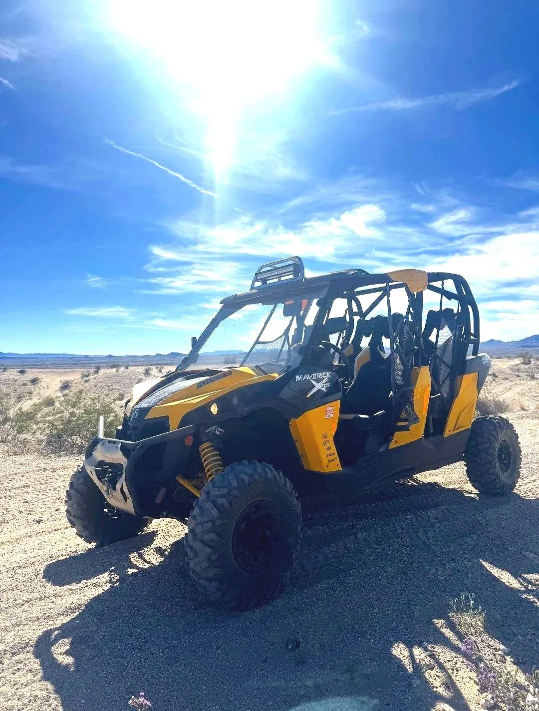 Yellow and black off-road vehicle parked in a desert landscape under a bright blue sky with the sun shining.