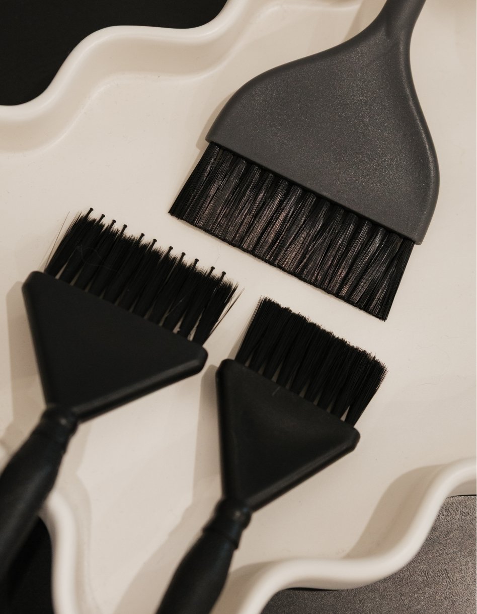 A pair of black eyelash brushes and a small cleaning brush, all placed on a white surface.