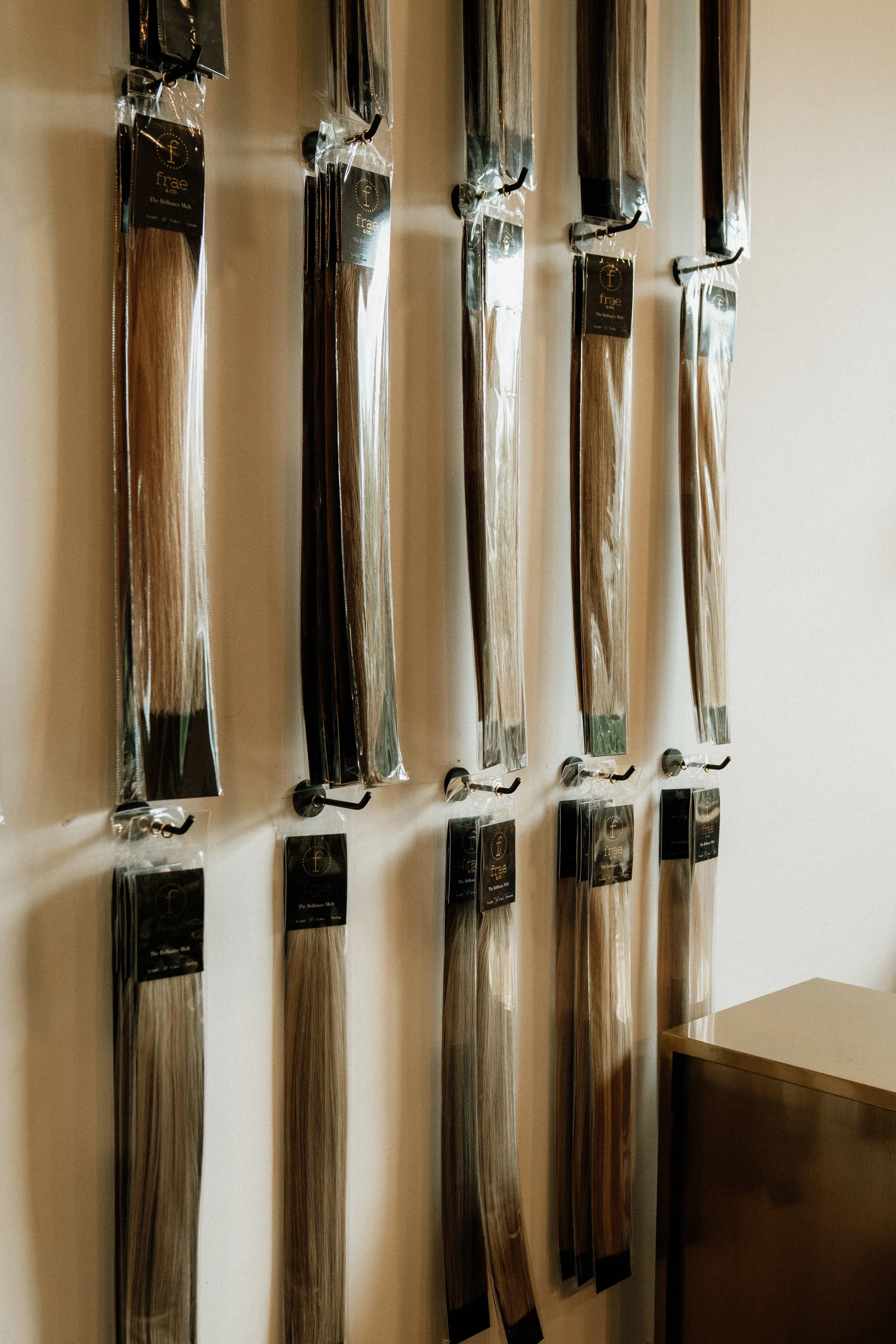 Multiple long, straight hair extensions in clear packaging hanging on hooks on a wall.