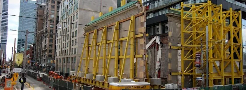 Historic building wall supported by a large steel retention structure during Ontario Line construction in downtown Toronto.