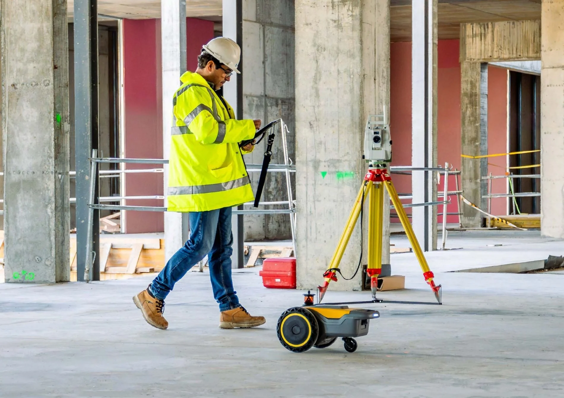 Construction worker operating an HP SitePrint robotic layout printer inside an unfinished building