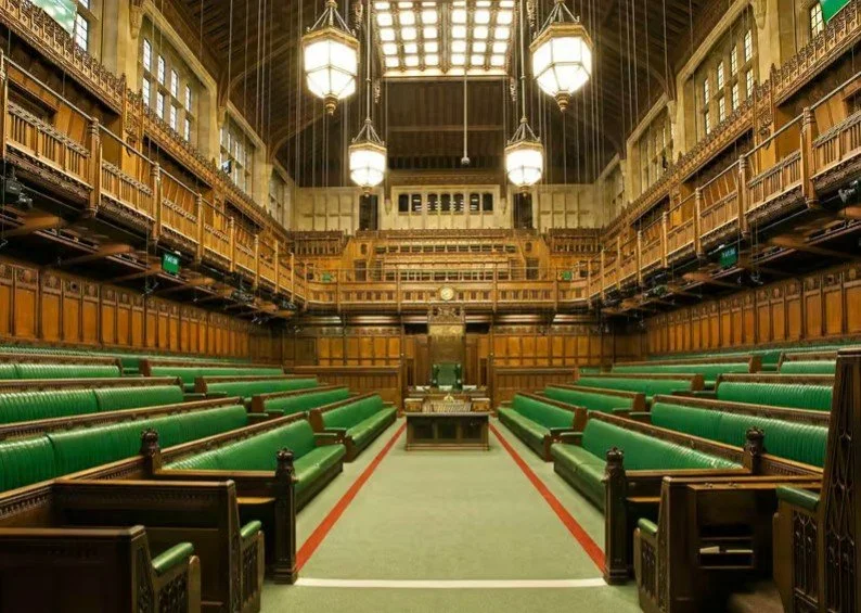 Interior of the House of Commons chamber showing its green benches, wooden galleries and Speaker's chair inside the Palace of Westminster.