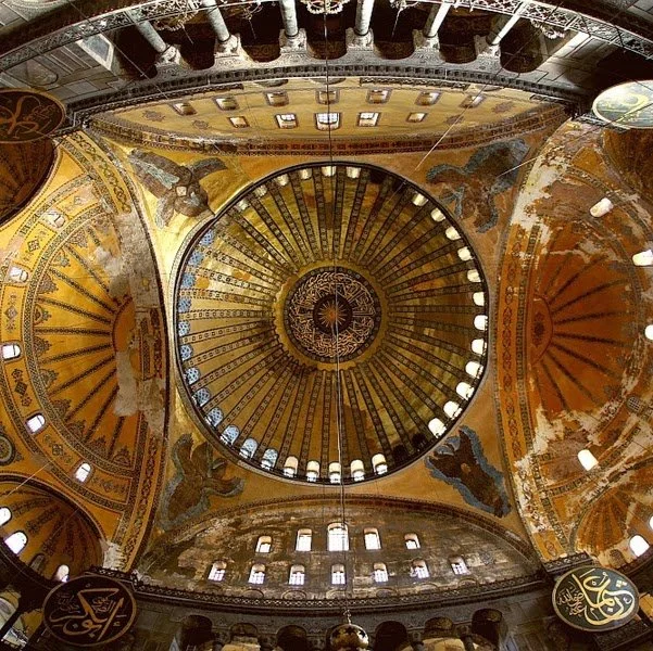 Interior of Hagia Sophia looking upward at the central dome, surrounding arches, windows and historic decorative surfaces.