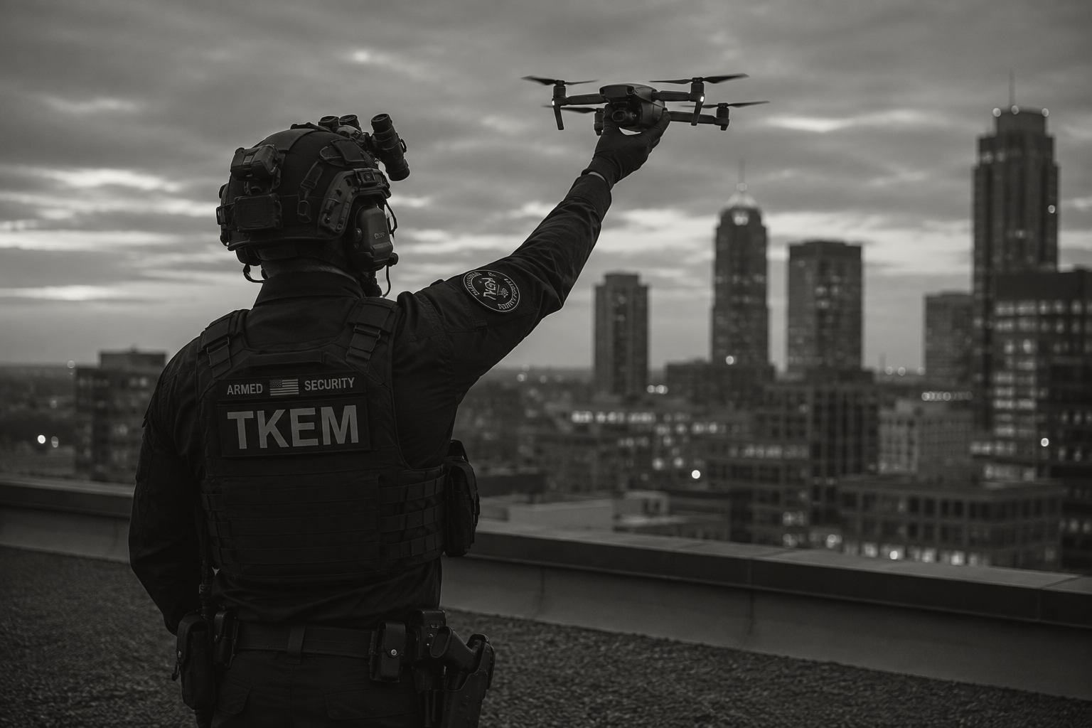 A security officer on a rooftop holding a drone against a city skyline at sunset, wearing tactical gear and a vest labeled 'TKEM'.