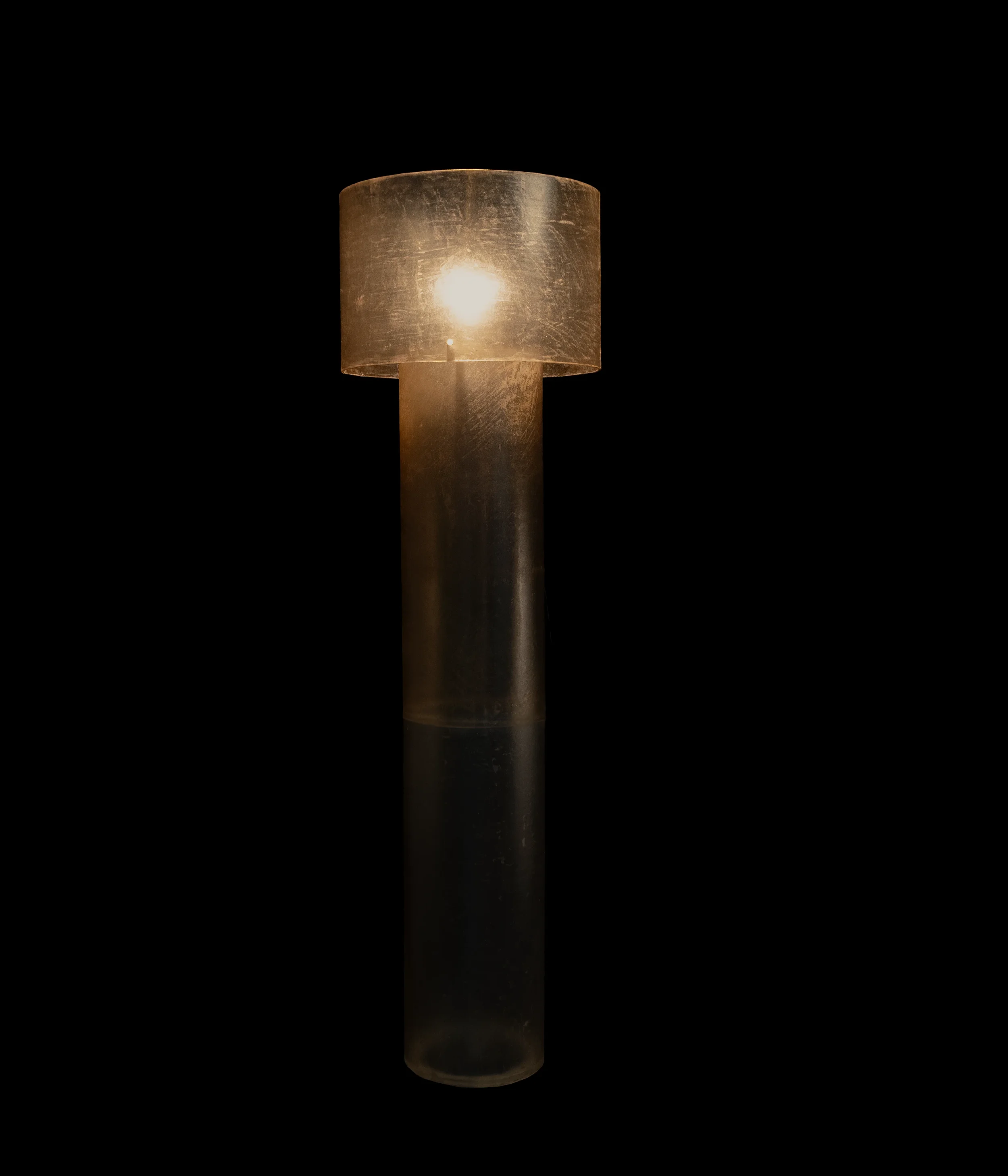 Tall monolithic floor lamp in dark hand-stitched leather, standing as a collectible art object in a dark interior.