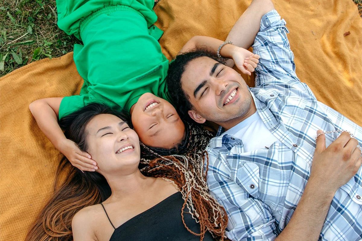A happy family of three lying on a blanket outdoors, smiling and relaxing.