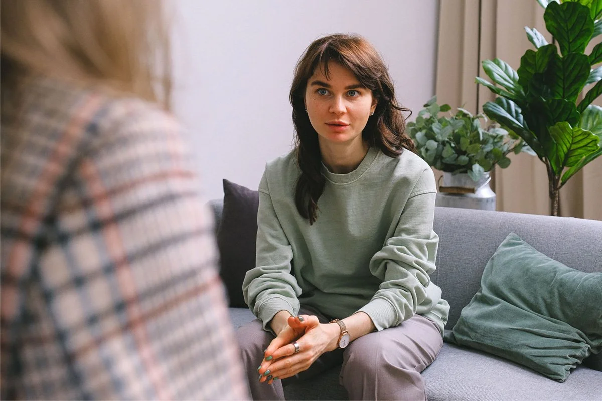 A person sitting on a gray couch, engaging in conversation with a therapist.
