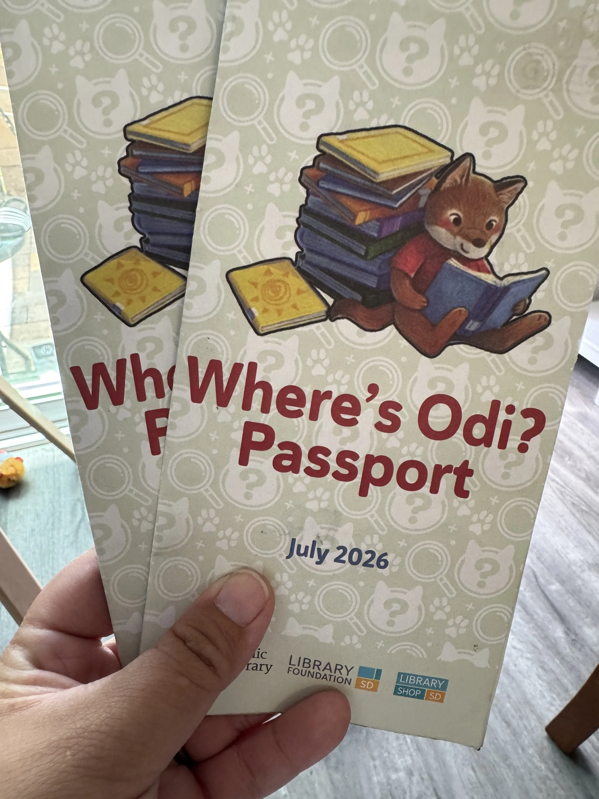 Two library Where's Odi? Passports for 2026 with colorful book illustrations and Odi the Coyote reading a book.