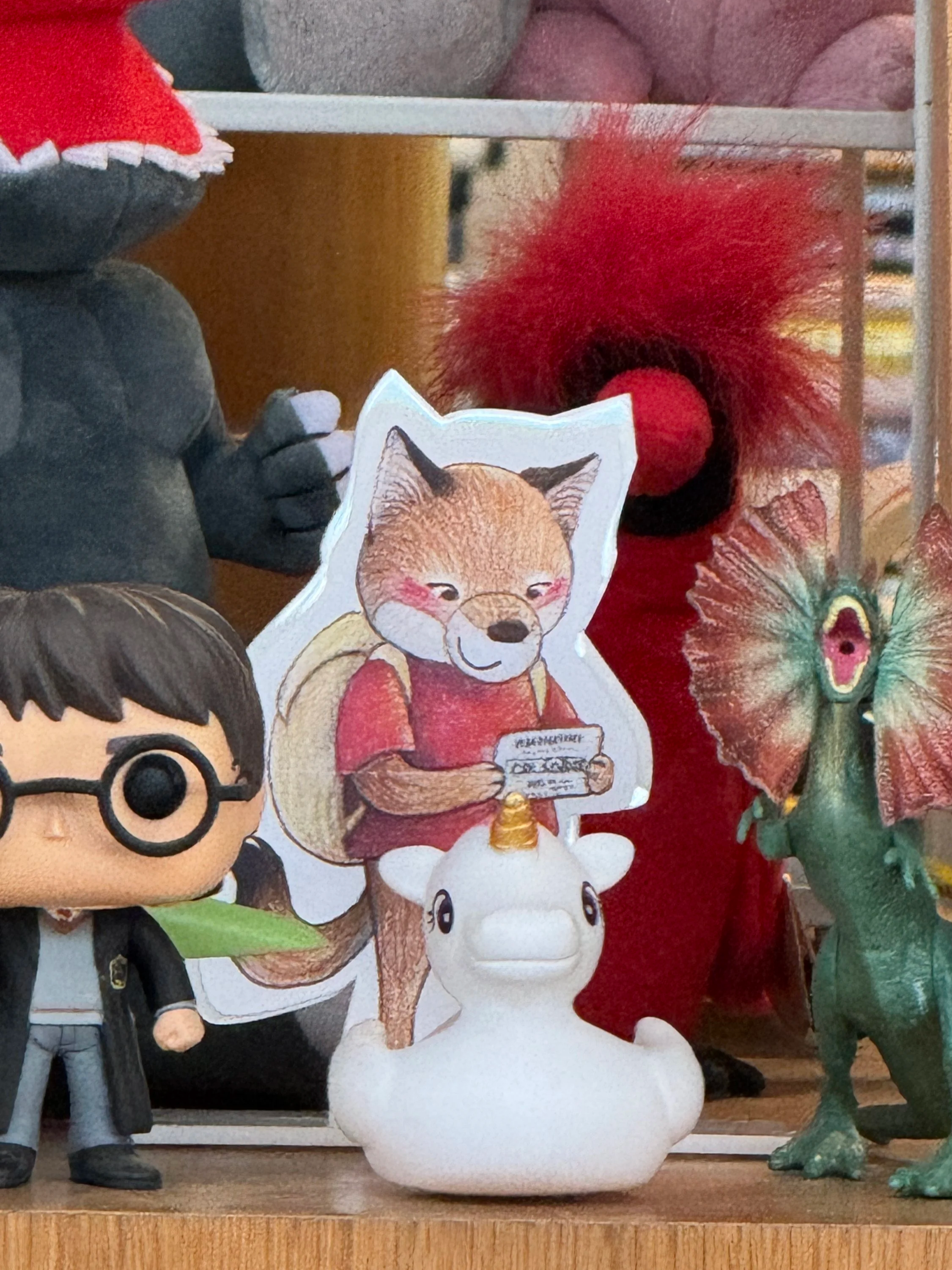Collection of figurines and novelty items, including a Funko Pop, a coyote holding a library card, a unicorn, and various colorful decorative pieces.