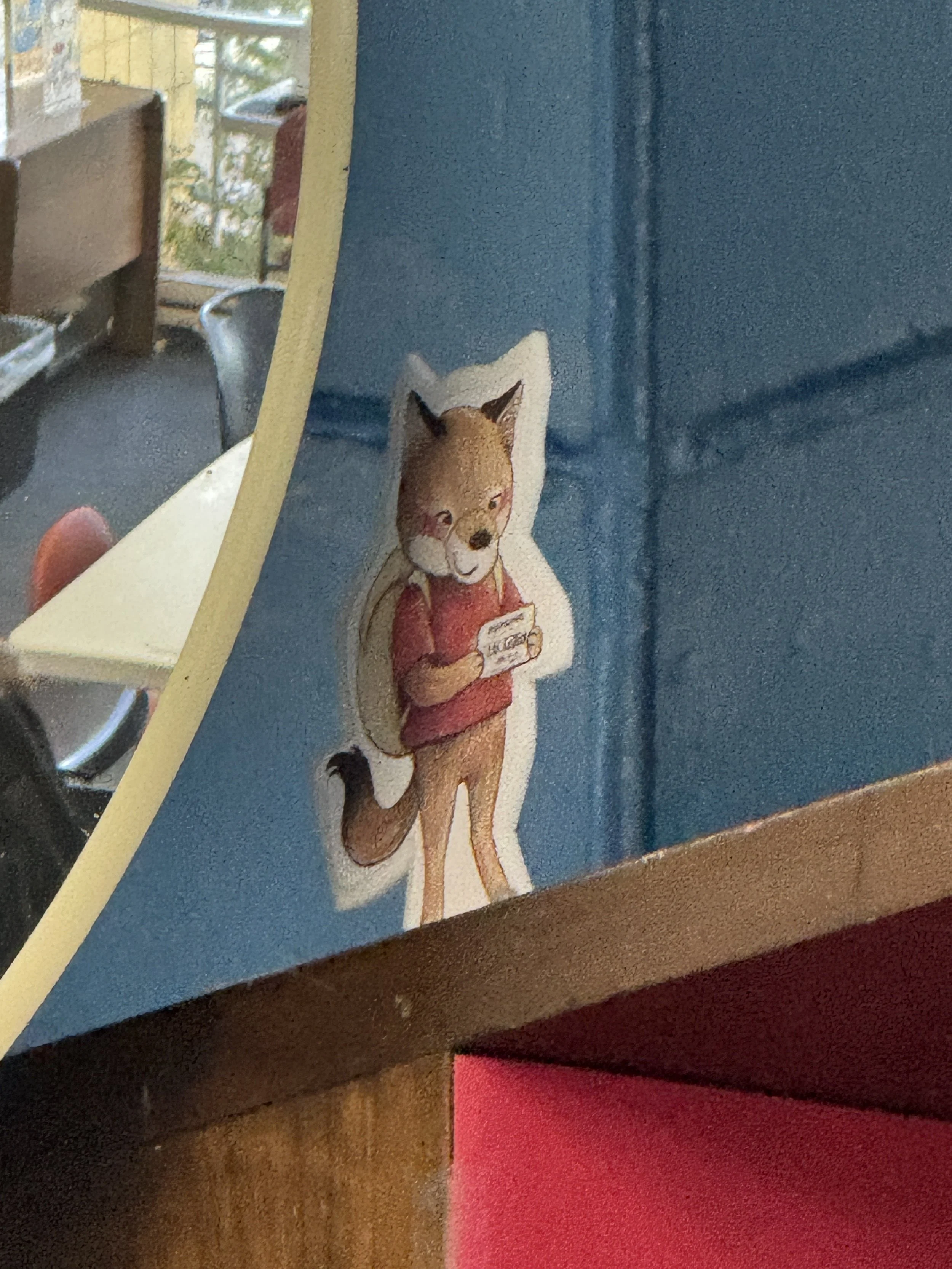 A painted figure of Odi the Coyote holding a library card near a corner of a room.
