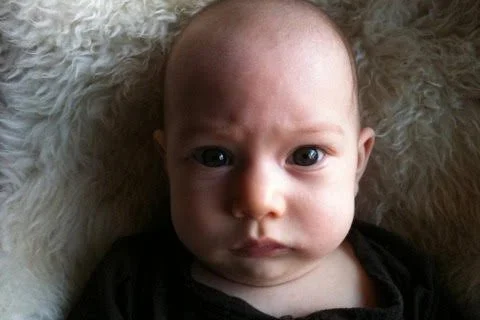 Close-up of a baby lying on a fluffy surface, looking directly at the camera with a serious expression.
