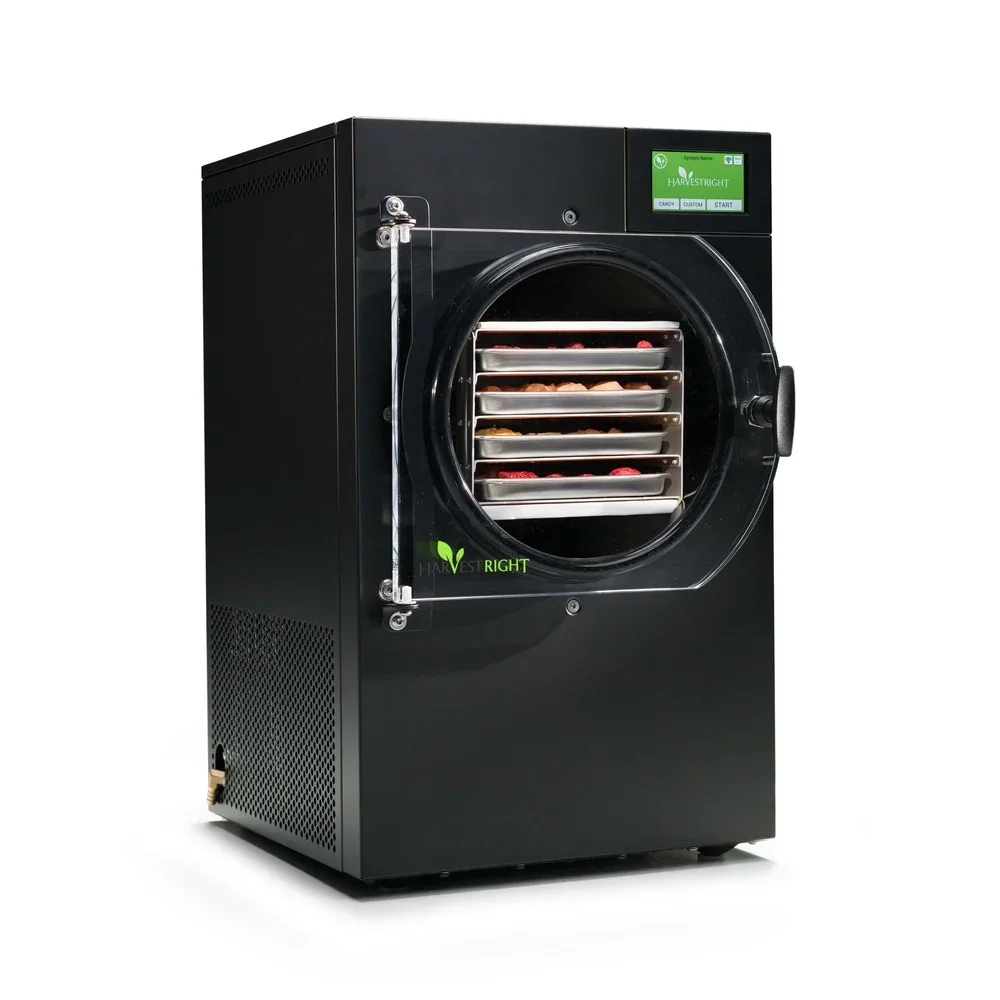 Black food dehydration or freeze-drying machine with a transparent door, showing trays of dried fruit inside, digital control panel on the top right.