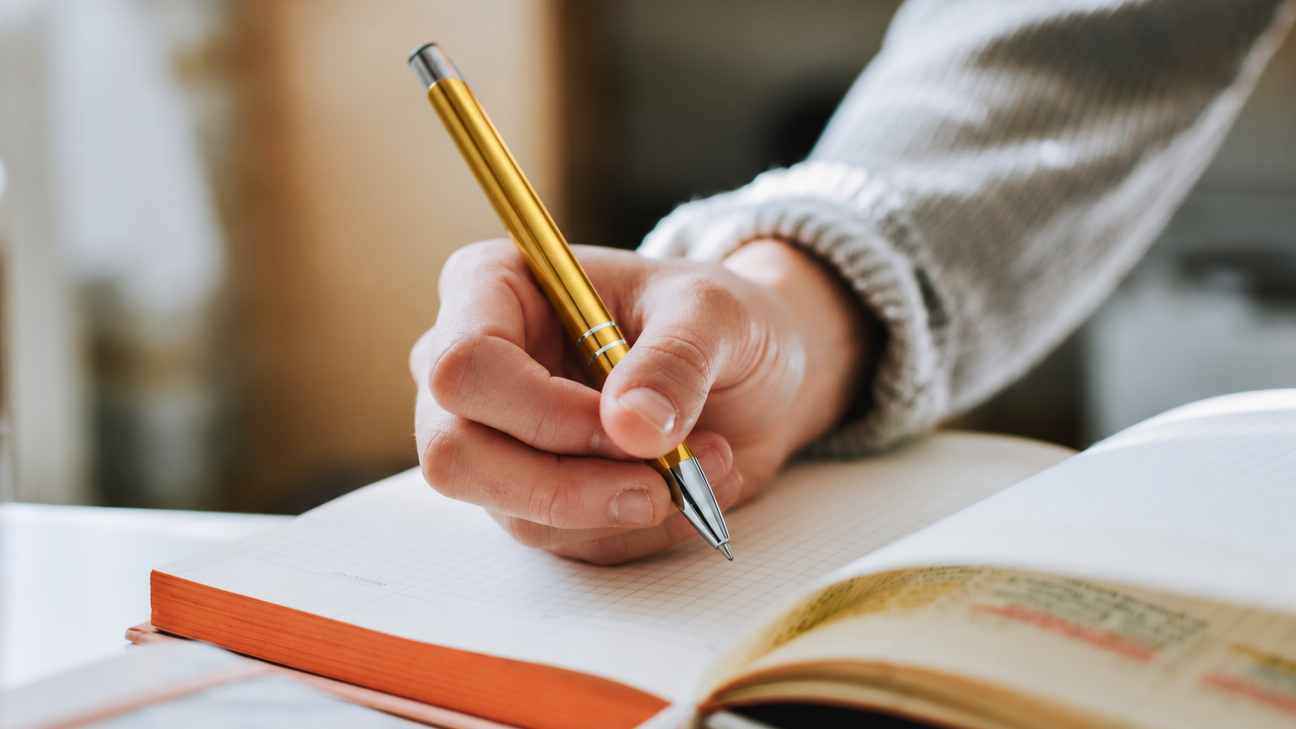Person taking notes beside an open book.