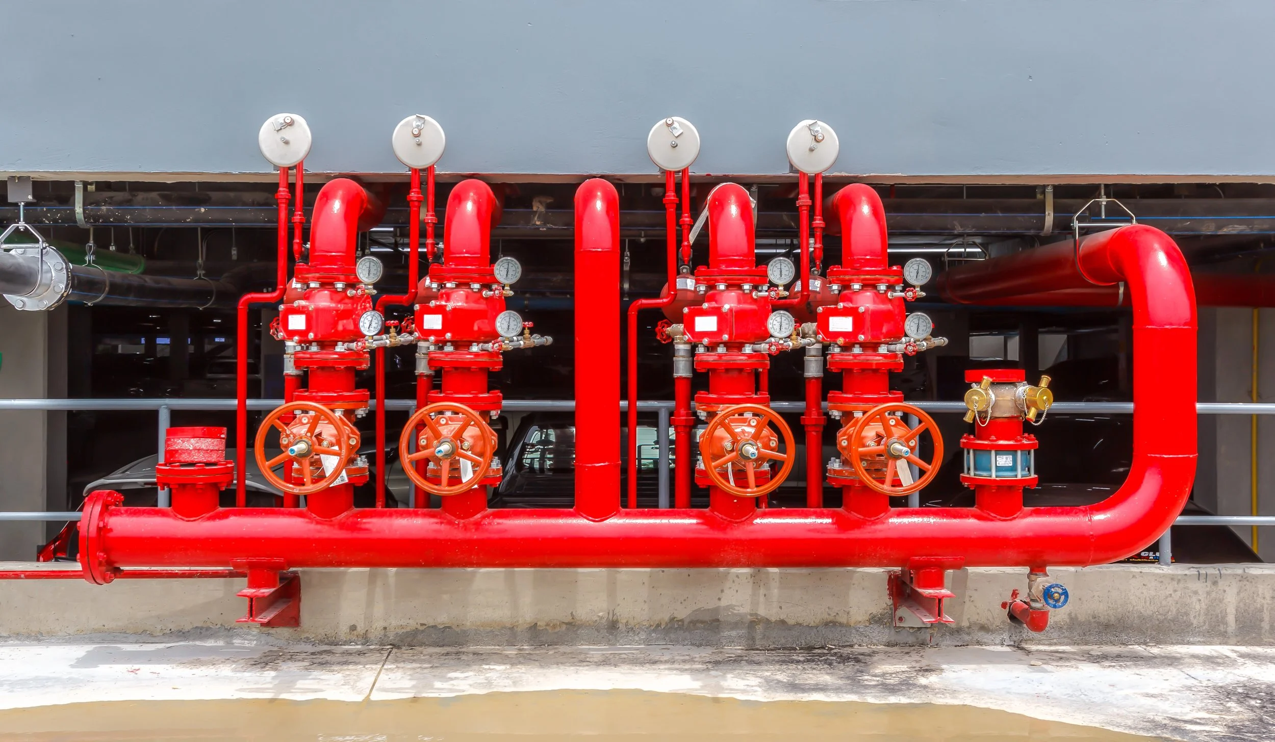Fire suppression system with red pipes, valves, and gauges mounted on a building exterior.