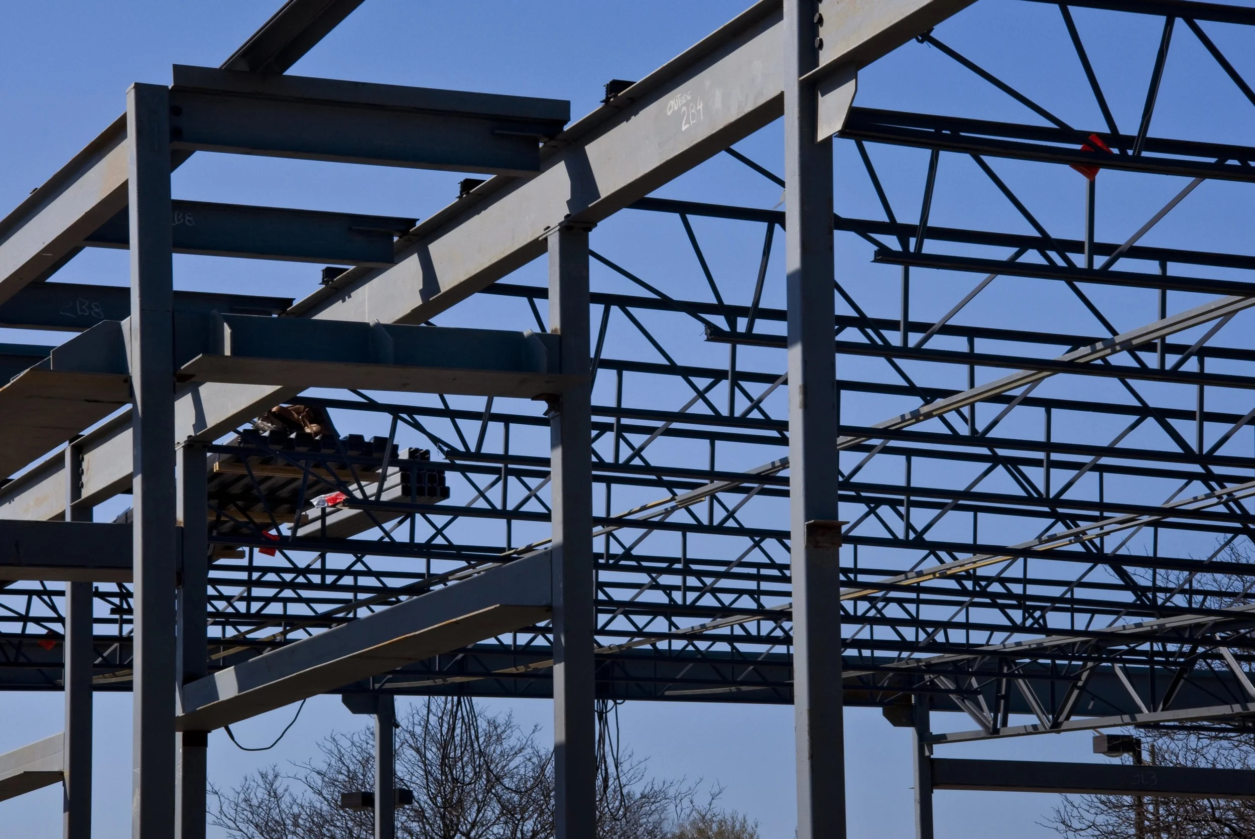 Metal framework of a building under construction with a clear blue sky in the background.