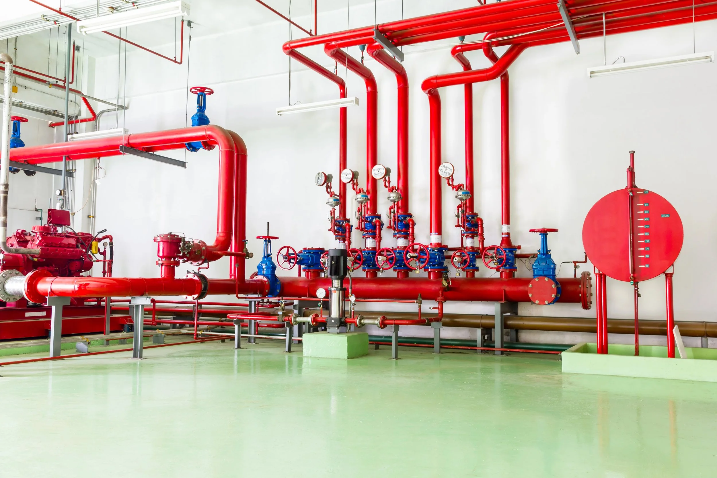 Fire sprinkler system with red pipes, gauges, and valves in a building's utility area.