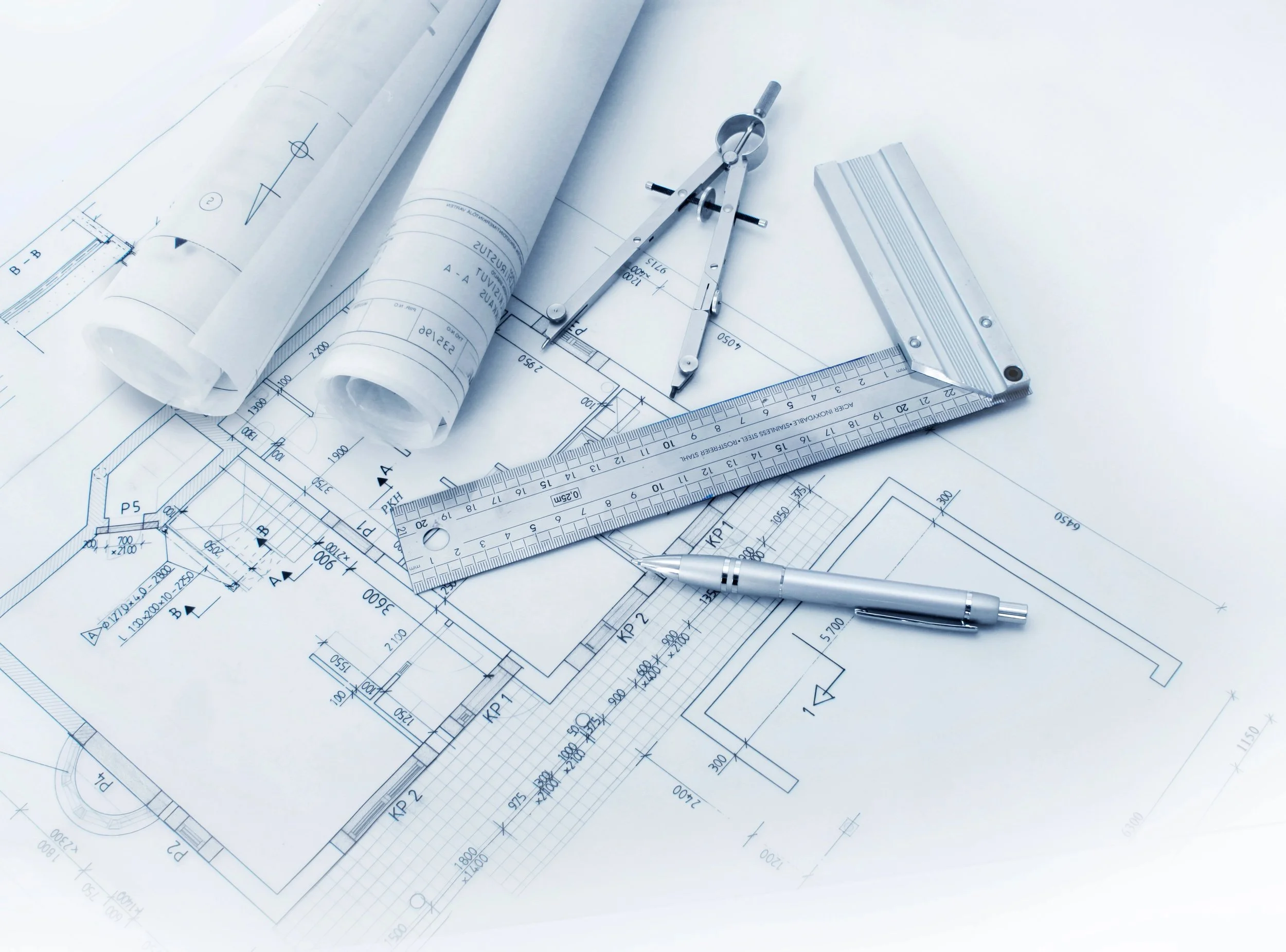 Blueprint drawings of a building or architectural design spread out on a white surface with a metallic compass, a ruler, and a pen.