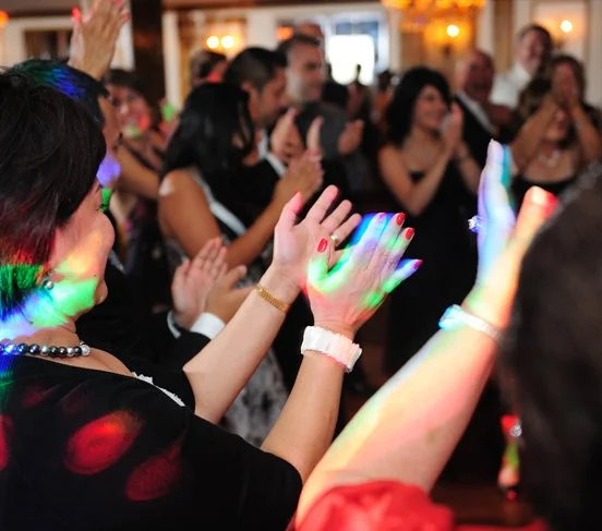 People clapping and dancing at a lively event with colorful lights and a festive atmosphere.