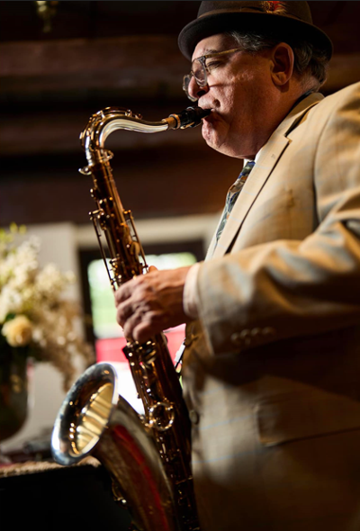 A man in a beige suit and black hat playing a saxophone