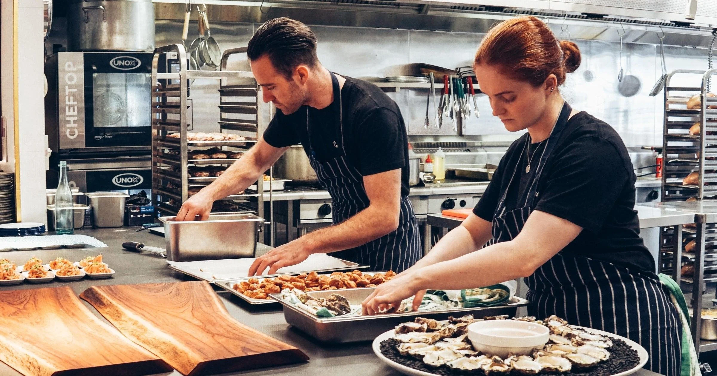 man and woman working in a commercial kitchen preparing food trays