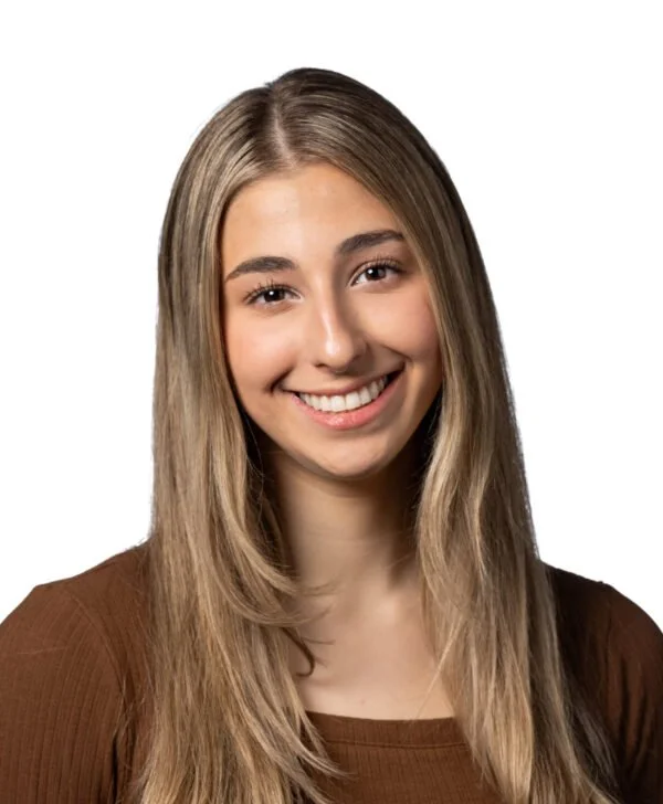 A young woman with long blonde hair smiling, wearing a brown top, against a white background.