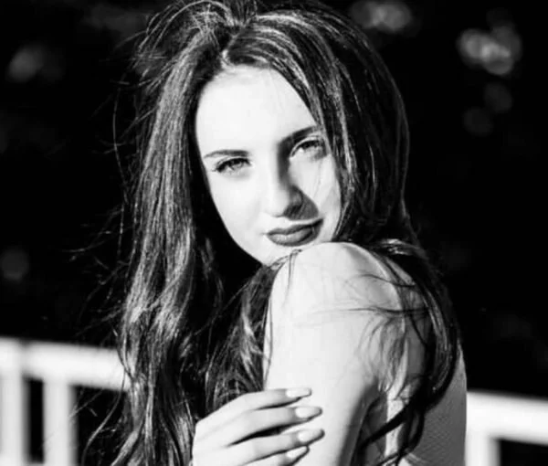 Black and white photograph of a young woman with long hair, looking at the camera, outdoors.