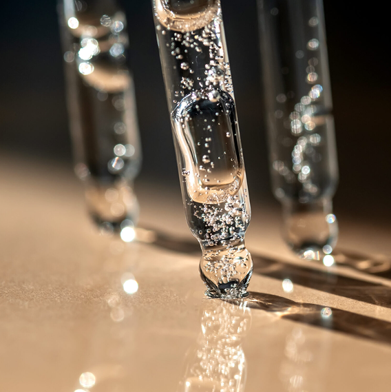 Close-up photo of glass test tubes with bubbles, standing on a reflective surface with light reflections.