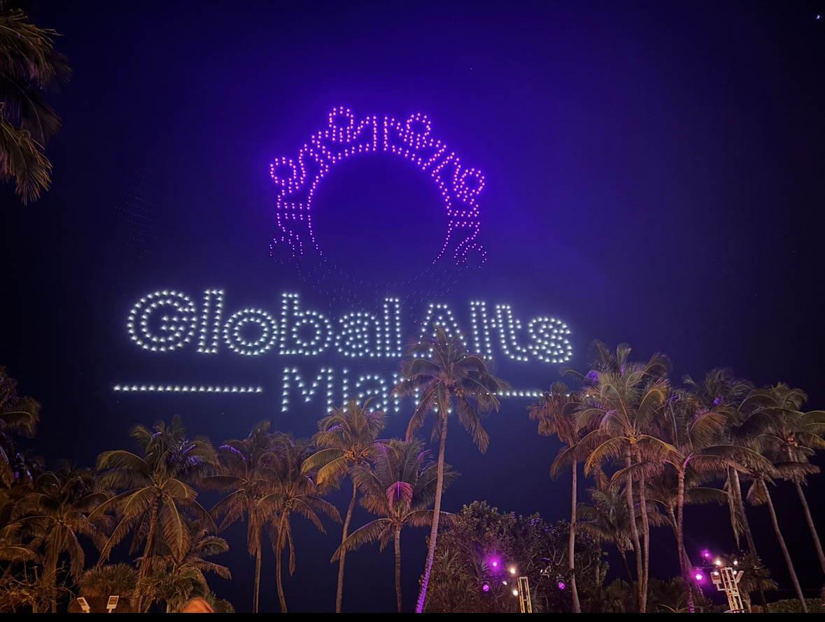 Nighttime aerial fireworks display spelling out 'Global Alts Miami' with palm trees in foreground.