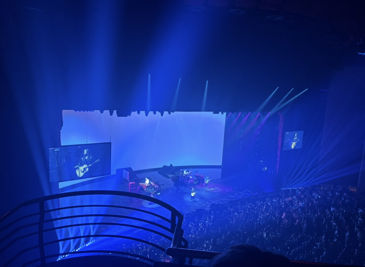 A concert stage illuminated with blue lights, with musicians performing and a large audience watching.